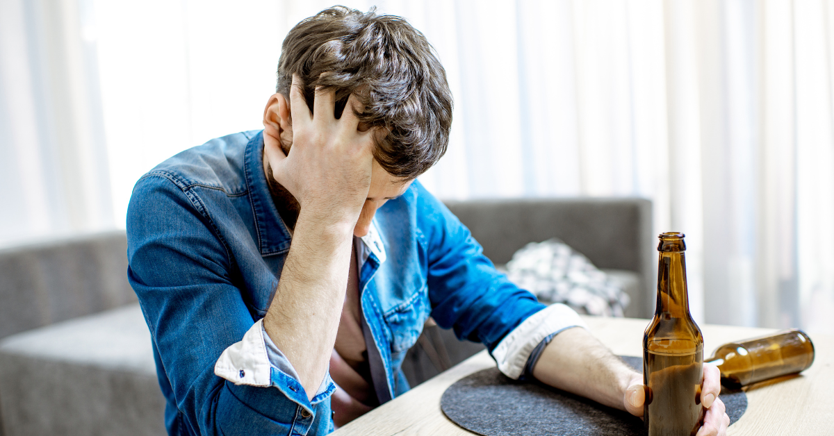 Man with alcohol use disorder in need of alcohol addiction treatment with two beers in front of him and his head in his hand as he clasps the bottle of beer