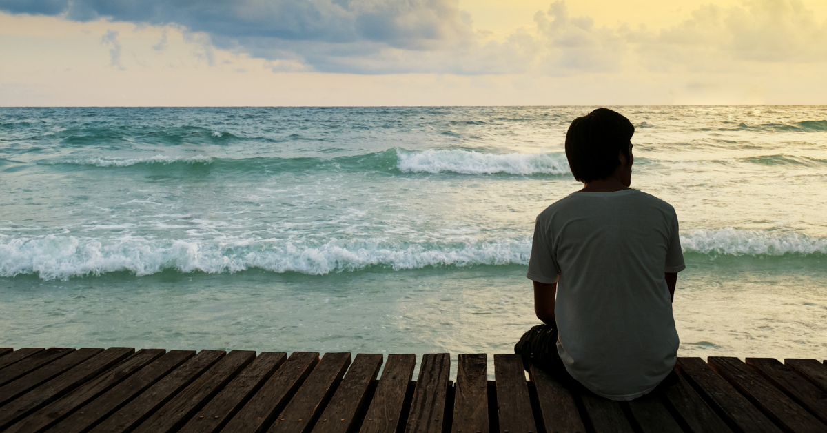 A man sitting by himself on a boardwalk looking at the ocean dealing with loneliness and addiction