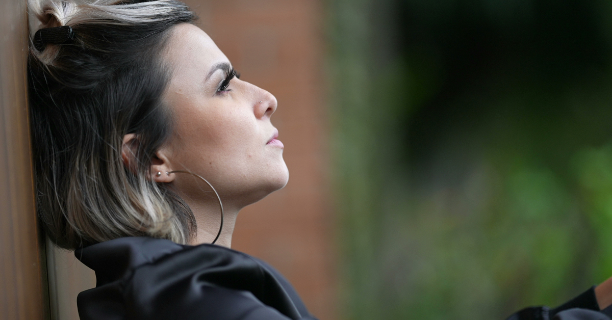 A woman sitting against a fence with her head leaned back dealing with shame and guilt in recovery