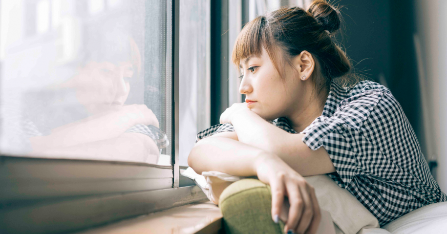 A woman looking out a window with a forlorn look on her face, she is struggling with wanting to relapse