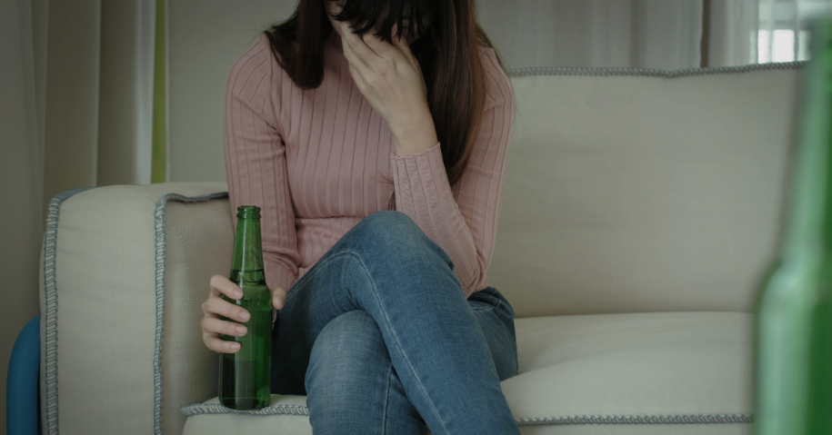 Woman holding alcohol bottle with head in hands