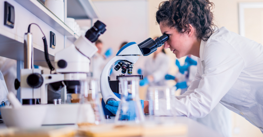 Woman researcher with curly hair looking into a microscope in a research lab researching naltrexone for meth addiction treatment